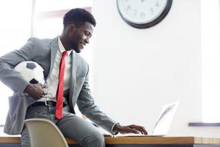 Man holding a soccer ball while using laptop