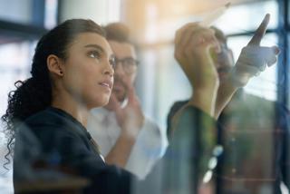 Shot of a group of colleagues brainstorming together on a glass wall in an office